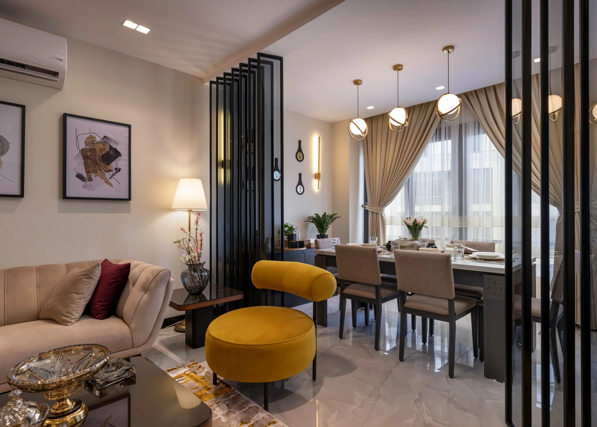 A living and dining space is designed by Aghbary Tex in Egypt. A beige sofa and a yellow chair are placed in the living area. A black room divider is set between the two spaces. A dining table with beige chairs is arranged near a window