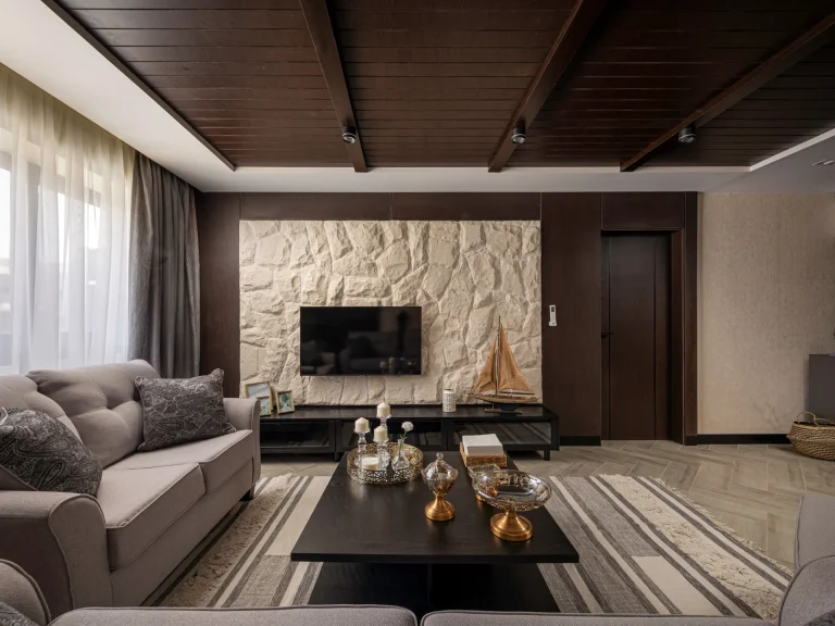 A living room interior designed by Aghbary Tex in Egypt. A beige sofa is placed on the left side. A stone wall with a television is set in the center. A black coffee table is arranged in front of the sofa